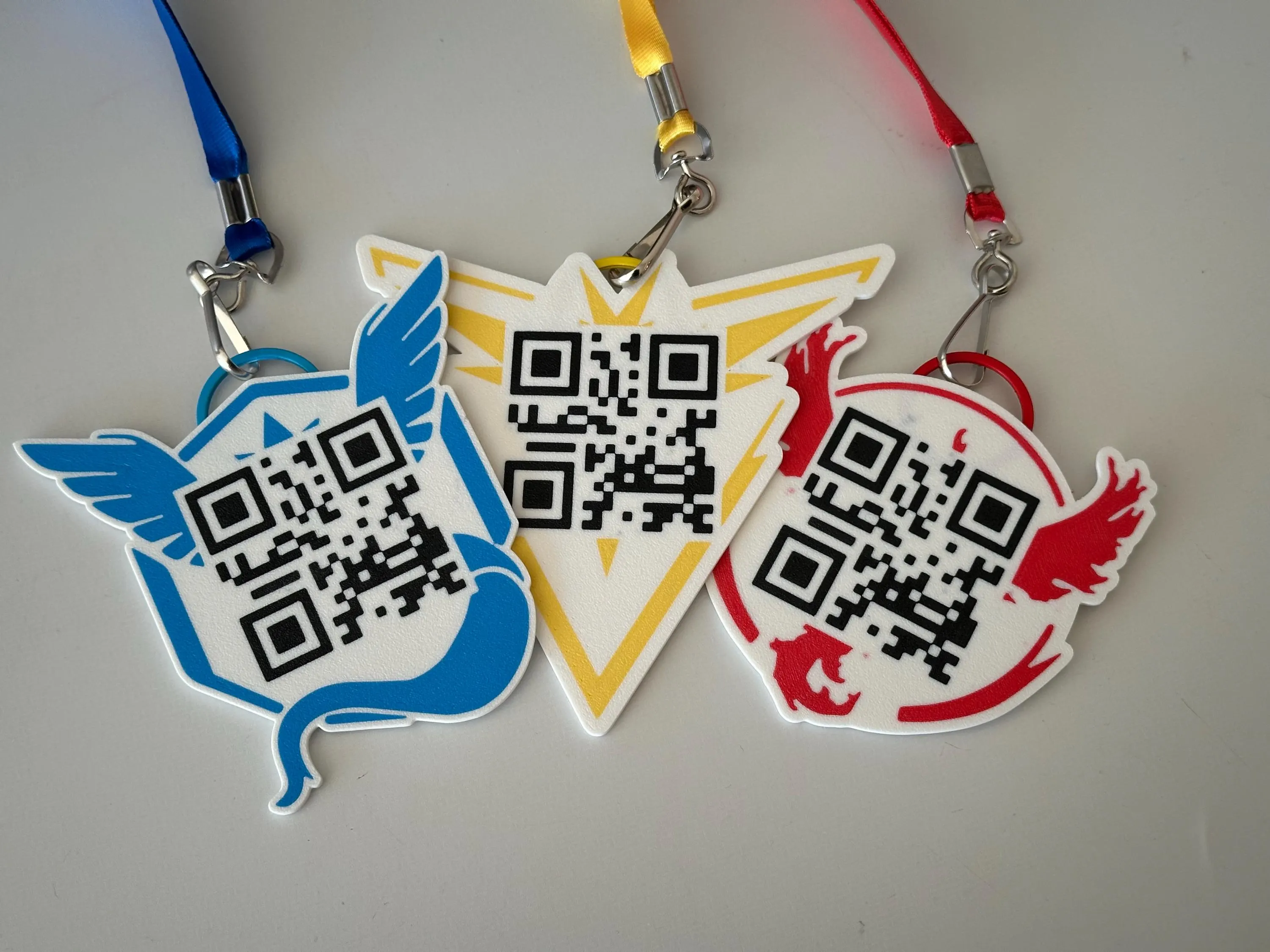All three team badges together, each printed with a scannable QR code, on blue, yellow, and red lanyards